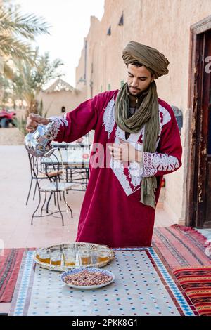 Un homme marocain habillé traditionnellement verse des verres de thé à la menthe pour servir avec des collations Banque D'Images