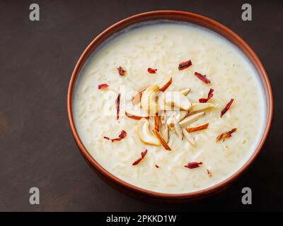 Kheer de riz crémeux garni de noix et d'hibiscus. Bol avec riz au lait sur fond sombre. Vue de dessus Banque D'Images