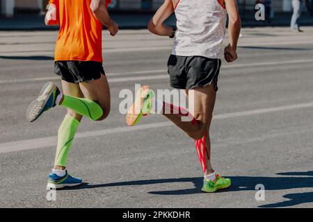 dos deux athlètes coureurs course marathon en ville, jambes homme jogger dans les manches de compression et muscle kinésiotapage de mollet Banque D'Images