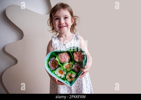 Petite fille en forme de coeur tient boîte en forme de coeur avec des guimauves maison, doux dans les mains. Produits écologiques faits maison sans sucre. Cadeau comestible, bouquet Banque D'Images