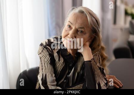 Portrait souriant d'une femme âgée heureuse souriant et assise à la maison Banque D'Images