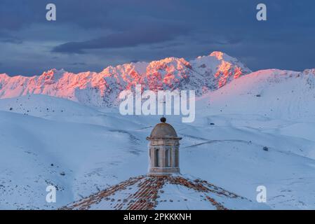 Vue rapprochée du toit de l'église de Santa Maria della Pieta avec des montagnes enneigées de Gran Sasso illuminées au coucher du soleil, Rocca Calascio Banque D'Images