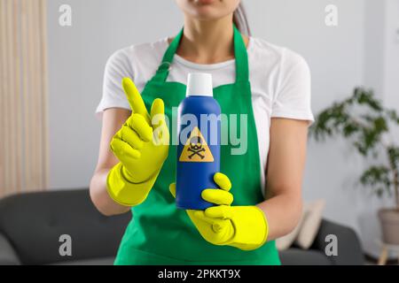 Femme montrant une bouteille de produit chimique toxique domestique avec un panneau d'avertissement, gros plan Banque D'Images