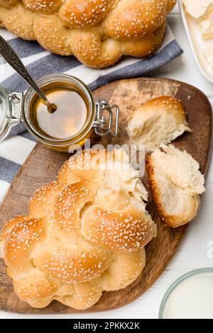 Pain tressé fait maison avec graines de sésame, beurre et miel sur table en bois blanc, plat. Challah traditionnel Banque D'Images