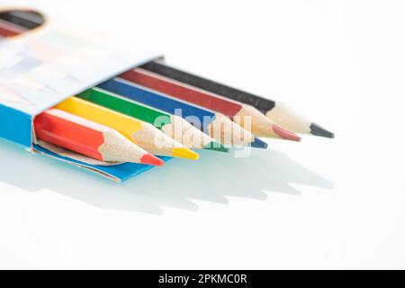 Thème Office. Les crayons de couleur dans une boîte ouverte se trouvent sur un fond miroir blanc Banque D'Images