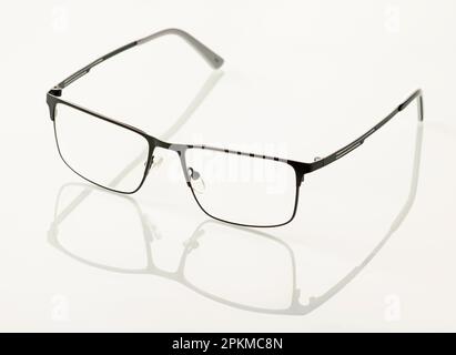 Les lunettes dans un cadre métallique noir sont reflétées dans un fond miroir blanc Banque D'Images