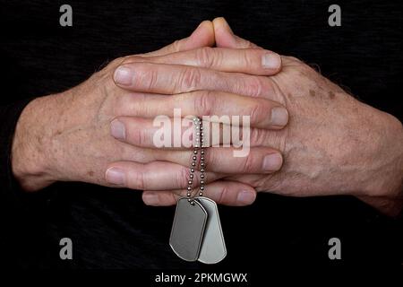 Gros plan des mains de l'homme accrochées dans la prière et tenant des étiquettes de chien militaire sur une chaîne Banque D'Images