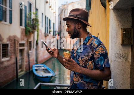 Un touriste utilise son smartphone pendant ses vacances à Venise, homme élégant avec de la crème glacée Banque D'Images