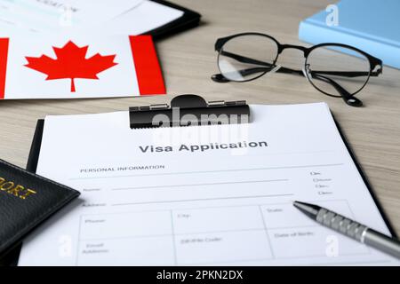 Formulaire de demande de visa pour l'immigration, le passeport, le drapeau canadien et les lunettes sur table en bois, en gros plan Banque D'Images