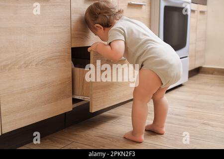 Petit enfant explorant le tiroir dans la cuisine. Situation dangereuse Banque D'Images