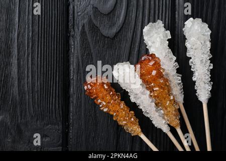 Bâtonnets avec cristaux de sucre sur table en bois noir, plat et espace pour le texte. Bonbons savoureux Banque D'Images