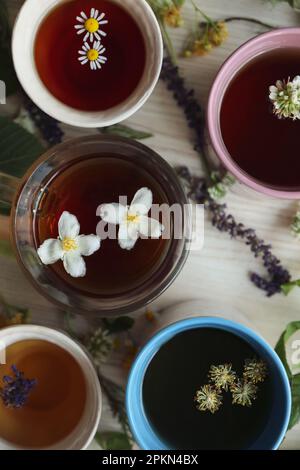 Différentes tasses de thé aromatique chaud et d'herbes fraîches sur une table en bois blanc, plat Banque D'Images