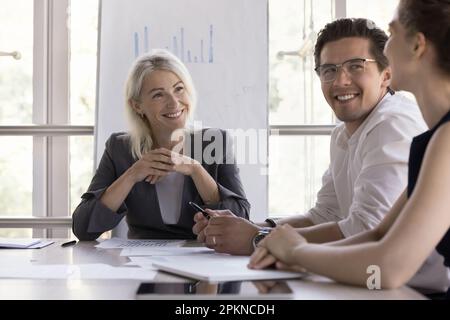 Une femme heureuse d'âge moyen à l'écoute des idées des jeunes employés Banque D'Images