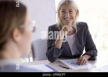 Une femme d'affaires mûre et confiante et gaie qui discute avec ses partenaires lors d'une réunion de négociation Banque D'Images