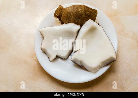 Trois pièces d'une noix de coco sèche sont dans une plaque blanche sur un comptoir en carreaux blancs. Banque D'Images
