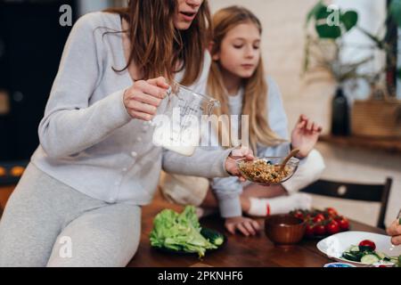 La mère verse du lait dans un bol de granola Banque D'Images