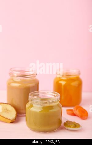 Bocaux en verre avec aliments nutritifs pour bébé sur fond rose. Purée de légumes et de fruits Banque D'Images