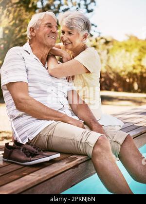 Faire de leur retraite une prudence toute aussi insouciante que possible. un heureux couple senior se détendant ensemble au bord de la piscine. Banque D'Images