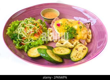 Œufs Benedict (œufs pochés) sur du jambon grillé avec sauce hollande sur des gaufres belges avec courgettes grillées Banque D'Images