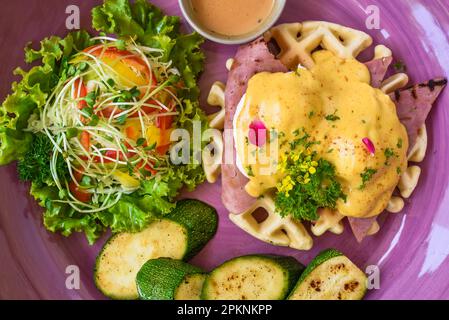 Œufs Benedict (œufs pochés) sur du jambon grillé avec sauce hollande sur des gaufres belges avec courgettes grillées Banque D'Images