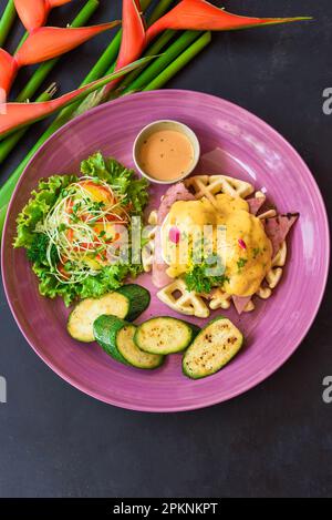 Œufs Benedict (œufs pochés) sur du jambon grillé avec sauce hollande sur des gaufres belges avec courgettes grillées Banque D'Images