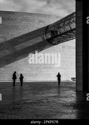 Un cliché vertical en niveaux de gris de plusieurs figures silhouettes debout sous un pont de verre Banque D'Images