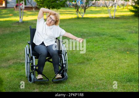 Femme caucasienne âgée faisant des exercices en étant assise dans un fauteuil roulant à l'extérieur. Banque D'Images