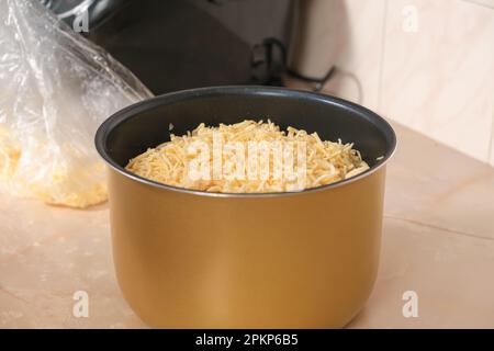 Un homme met du fromage congelé du congélateur râpé sur une râpe dans un bol de mijoteuse. multicuiseur. Déjeuner de cuisine dîner pour la famille à la maison. processus de cuisson Banque D'Images