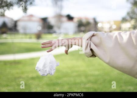 Main de femme blanche millénaire paresseuse jette des ordures en plastique sur l'herbe dans le parc, à l'extérieur, de près Banque D'Images