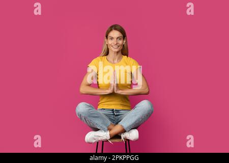 Joyeuse blonde européenne d'âge moyen, joyeuse, assise sur une chaise en position lotus, médite, profitez du calme Banque D'Images