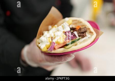 Un cuisinier grec a préparé un sandwich gyros traditionnel pour le déjeuner dans un restaurant. Ouvrier de cuisine cuisinant un plat de pita souvlaki enveloppé avec de la sauce tzatziki et de la viande Banque D'Images