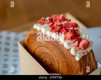 Gros plan de fraises rouges glacées et de crème douce sur un gâteau brun ou un croissant, dessert sucré sur une table en bois au café. Banque D'Images