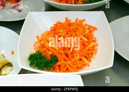 salade de carottes et de persil dans une assiette blanche servie sur un comptoir de cantine. Banque D'Images