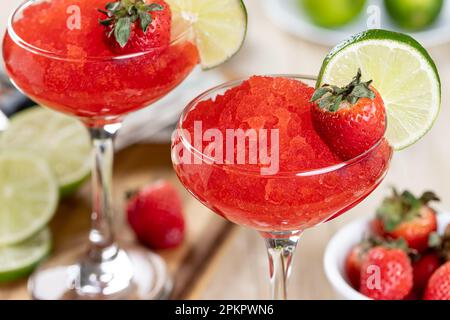 Gros plan de daiquiri aux fraises surgelées garni de fraises et de tranches de lime sur une table en bois Banque D'Images