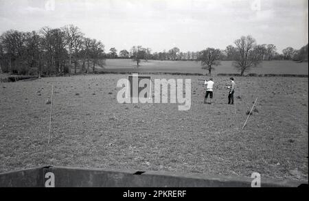 Années 1960, historique dehors dans un champ, deux hommes avec des fusils de campagne sur la pratique de tir ou peut-être faisans Angleterre, Royaume-Uni. Banque D'Images