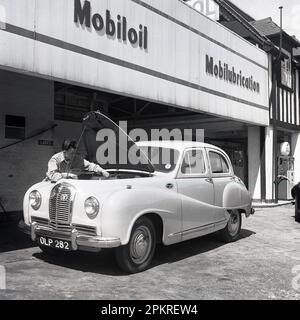 1950s, historique, un agent de service masculin nettoyant le pare-brise avant d'une voiture d'Austin, à la station de service de Ravenscroft, une nouvelle station de service et Mobilgas petriol, Londres, Angleterre, Royaume-Uni. Panneau sur le côté de la voiture britannique dit Austin/Angleterre, Banque D'Images