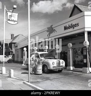 1950s, historique, automobile... Une voiture d'Austin dont l'huile a été changée par un préposé en uniforme à la station de service de Ravenscroft, une nouvelle station de service et de petriol de Mobilgas, Londres, Angleterre, Royaume-Uni. Sur la piste, le préposé de la station utilise l'équipement pour une vidange d'huile de 3 minutes. Banque D'Images