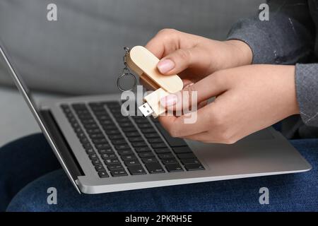 Femme avec ordinateur portable moderne et lecteur flash USB en bois assis sur un canapé, gros plan Banque D'Images