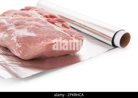 Rouleau de papier d'aluminium avec morceau de viande crue sur fond blanc, gros plan Banque D'Images