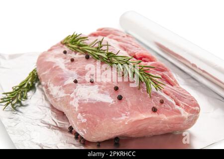 Rouleau de papier d'aluminium avec morceau de viande crue, romarin et grains de poivre sur fond blanc, gros plan Banque D'Images