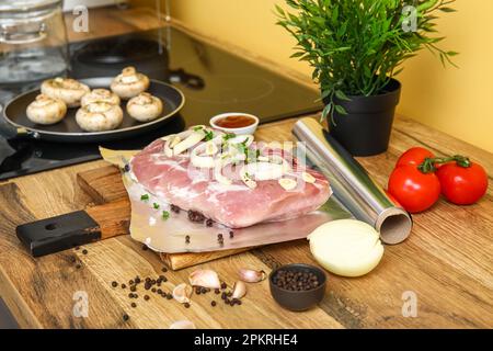 Rouleau de papier d'aluminium avec morceau de viande cru, épices et légumes sur une table en bois dans la cuisine Banque D'Images