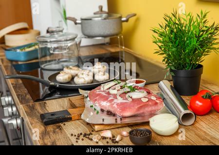 Rouleau de papier d'aluminium avec morceau de viande cru, épices et légumes sur une table en bois dans la cuisine Banque D'Images