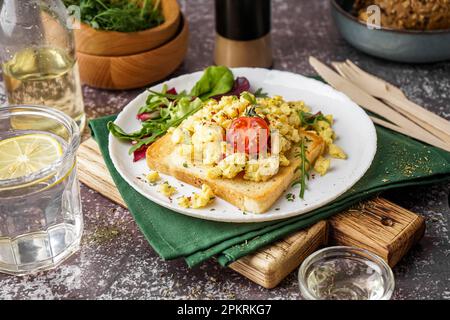 Assiette avec délicieux sandwich aux œufs brouillés et salade sur fond gris Banque D'Images
