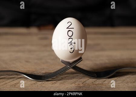 Un œuf de poulet blanc avec l'inscription 2023 se trouve sur deux fourchettes sur une table en bois à la maison Banque D'Images