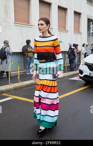 MILAN, ITALIE - 26 FÉVRIER 2023: Femme avec robe à rayures colorées en jaune, orange, turquoise, vert et noir sac Cambiaghi avant Luisa Spagnoli Banque D'Images
