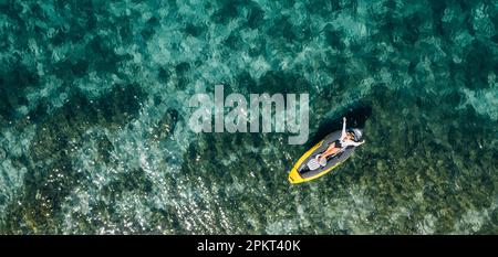 Une femme solitaire dans un chapeau de paille souriant, reposant couché flottant dans un kayak sur les vagues turquoises de la mer Adriatique. Vue aérienne du dessus de la côte. Exotique c Banque D'Images