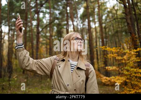 Femme à la recherche de la couverture mobile sur le téléphone mobile, aucun écran de service dans la forêt d'automne Banque D'Images