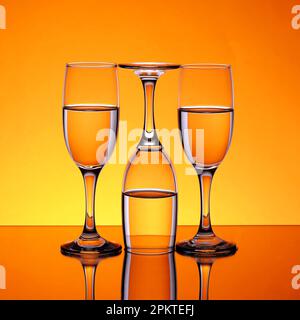 Gobelets en verre avec de l'eau, deux droits et l'autre inversé, sur un fond orange fragmenté Banque D'Images