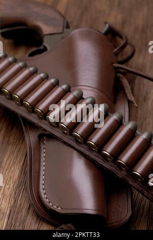 Ancienne ceinture de pistolet en cuir de l'ouest avec munitions et revolver dans un étui sur une table en bois Banque D'Images