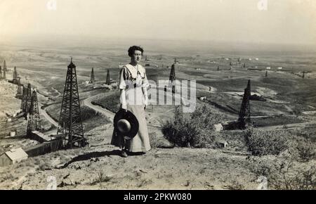 Oil Field, début 1900, puits de pétrole de Californie. Histoire de l'industrie pétrolière américaine. Femme debout devant Oil Field. Banque D'Images